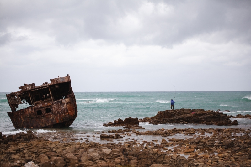 A man stands on the rocks near a shipwreck to fish
